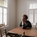 Worried man sitting at dining room table, holding his face with his hand.