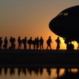 Silhouette of soldiers above to board a plane with the sun in the background.