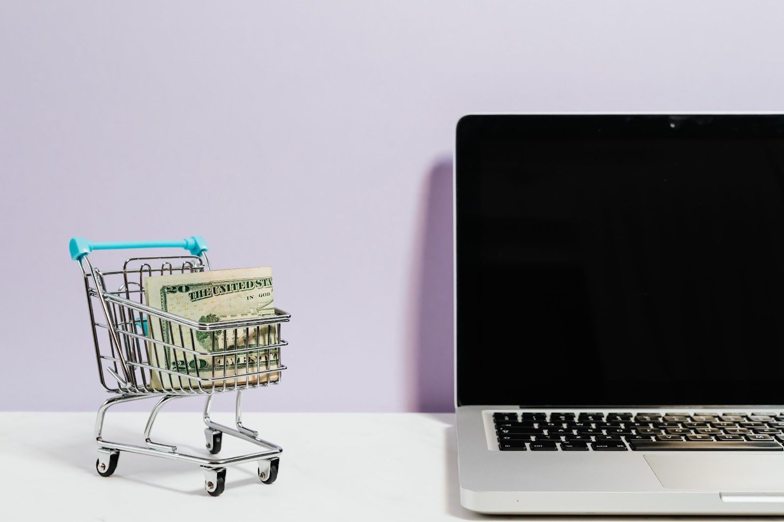 Toy shopping cart filled with dollar bills next to a laptop.