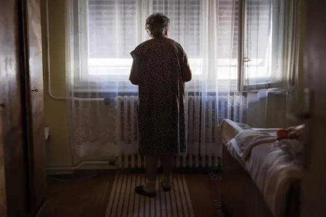 Understaffing a nursing home as a woman stands by a window alone.