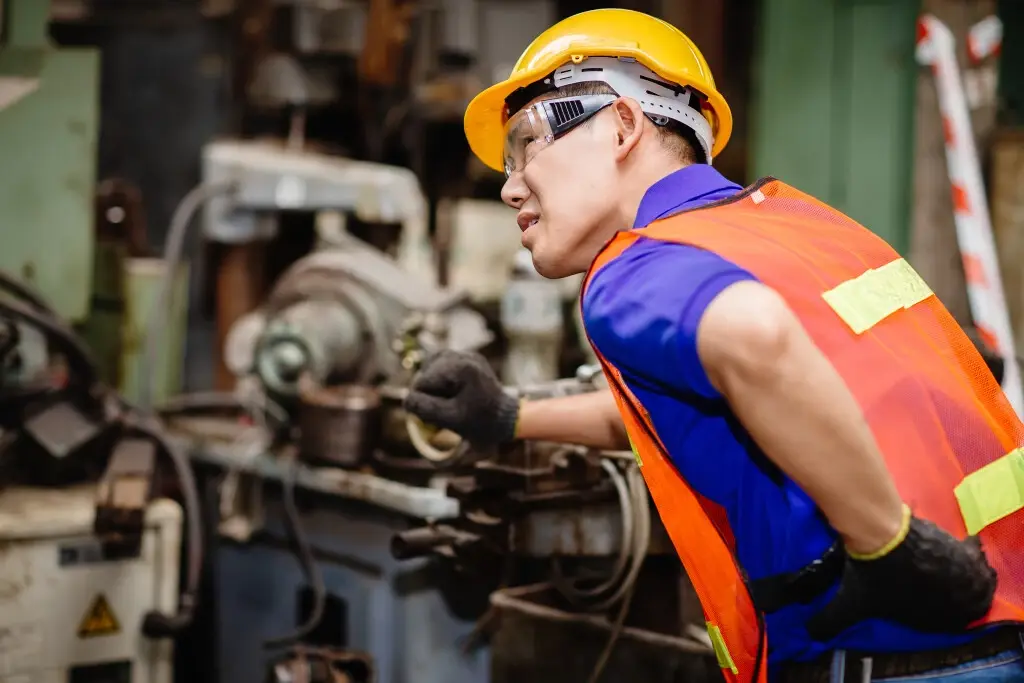 A worker in a machine factory feeling his back from an injury outside of work.