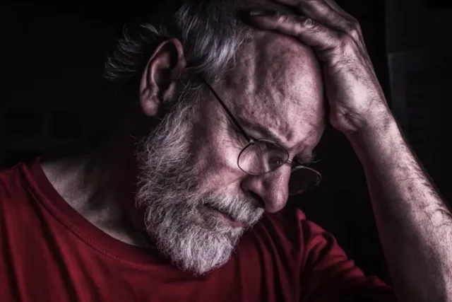 An old man putting his hand over his forehead, suffering emotional abuse in a Wisconsin nursing home.