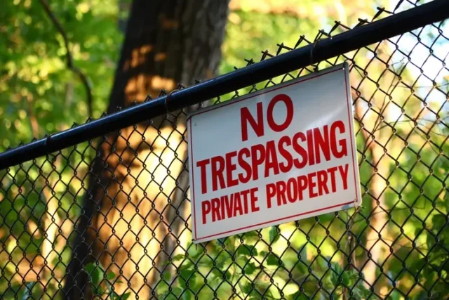 A sign that says "No trespassing private property" on a black fence. There are trees behind the fence.