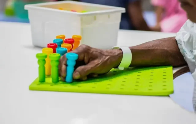 A brain injury victim putting colored pegs in a hole, doing occupational therapy.