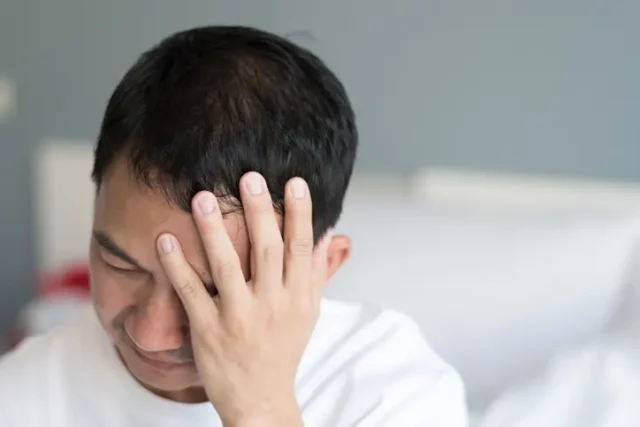 A man holding his head in pain, suffering from the long-term effects of a brain injury.