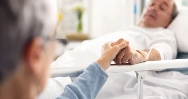 An old man experiencing minimal consciousness, holding a woman's hand on a hospital bed.