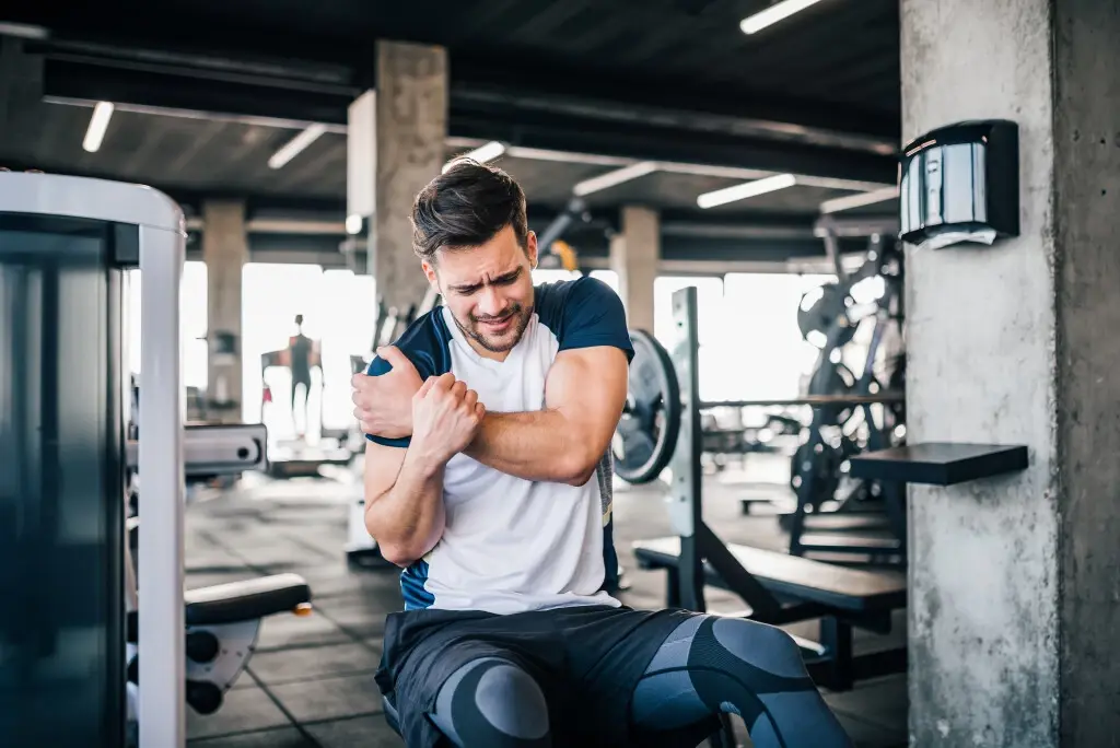 Someone getting injured in the gym, holding his shoulder after a workout.