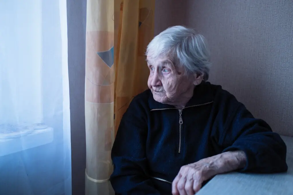An old woman looking outside a window, suffering nursing home abuse in Arizona.