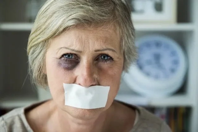 An old woman with a black eye and tape over her mouth, suffering from nursing home physical abuse.