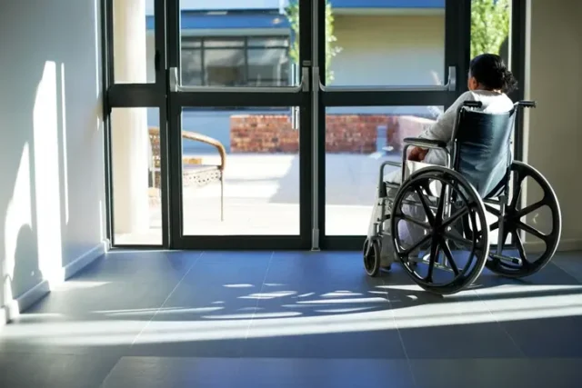 A wheelchair-bound nursing home resident looking out of a window, suffering from nursing home negligence.