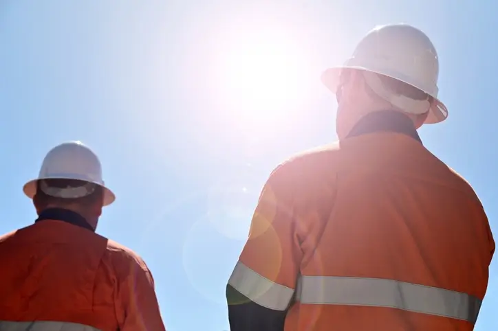 Two construction workers under the sun, working under extreme heat.