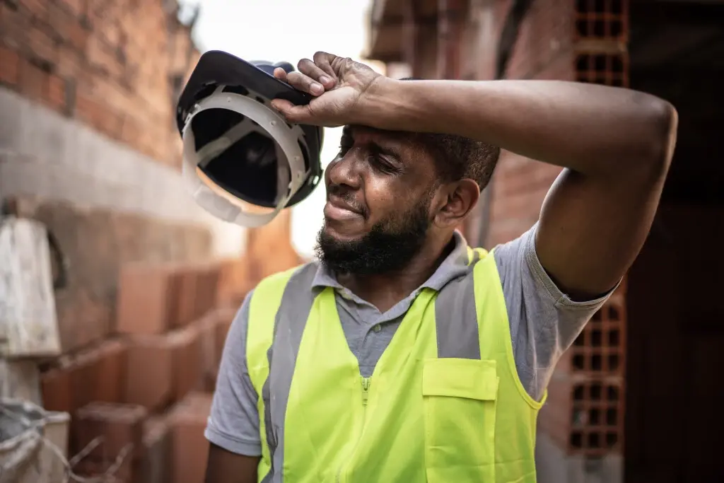 A construction worker putting his arm over his forehead, wondering what temperature he can legally leave work.